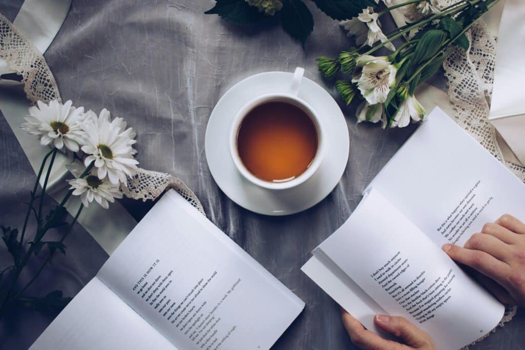 White ceramic teacup with saucer near two books above gray floral textile