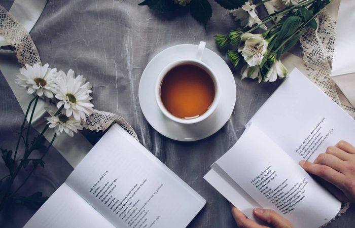 White ceramic teacup with saucer near two books above gray floral textile