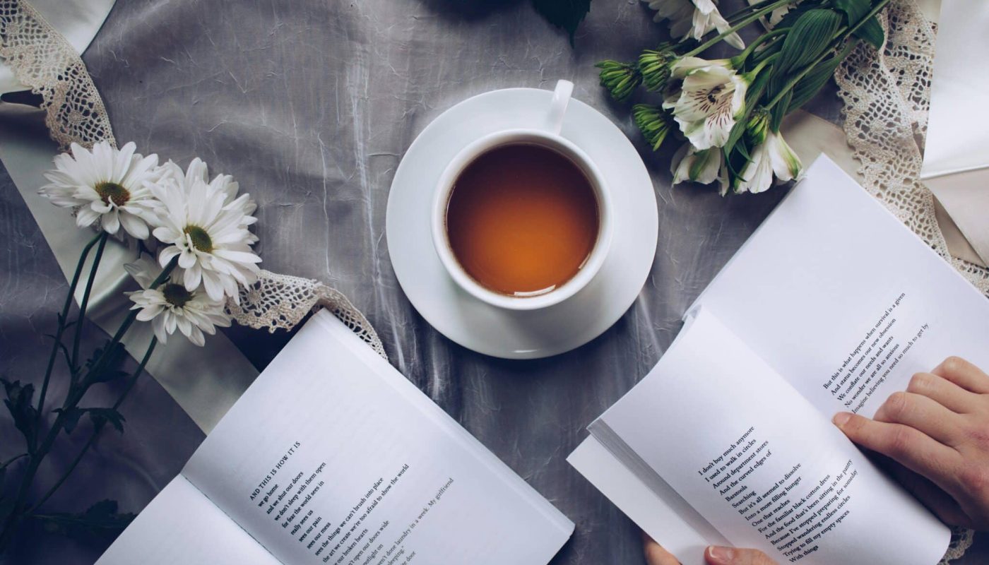 White ceramic teacup with saucer near two books above gray floral textile